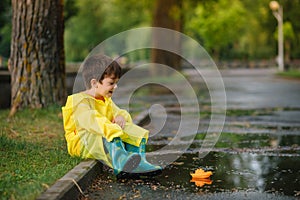 Child playing with toy boat in puddle. Kid play outdoor by rain. Fall rainy weather outdoors activity for young children