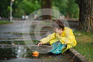 Child playing with toy boat in puddle. Kid play outdoor by rain. Fall rainy weather outdoors activity for young children