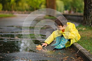 Child playing with toy boat in puddle. Kid play outdoor by rain. Fall rainy weather outdoors activity for young children