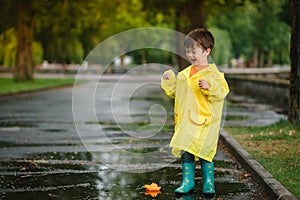 Child playing with toy boat in puddle. Kid play outdoor by rain. Fall rainy weather outdoors activity for young children
