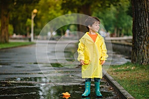 Child playing with toy boat in puddle. Kid play outdoor by rain. Fall rainy weather outdoors activity for young children