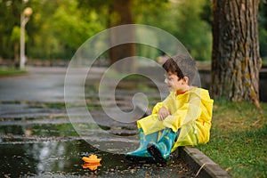 Child playing with toy boat in puddle. Kid play outdoor by rain. Fall rainy weather outdoors activity for young children. Kid