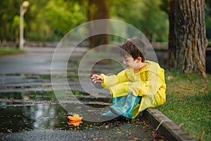 Child playing with toy boat in puddle. Kid play outdoor by rain. Fall rainy weather outdoors activity for young children. Kid