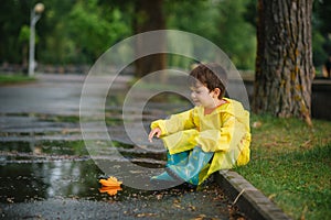 Child playing with toy boat in puddle. Kid play outdoor by rain. Fall rainy weather outdoors activity for young children. Kid