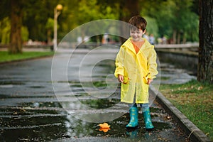 Child playing with toy boat in puddle. Kid play outdoor by rain. Fall rainy weather outdoors activity for young children. Kid