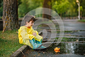 Child playing with toy boat in puddle. Kid play outdoor by rain. Fall rainy weather outdoors activity for young children. Kid