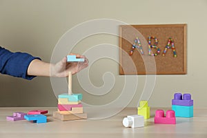 Child playing with toy pyramid at wooden table indoors, closeup. ABA therapy concept photo