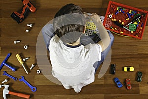 Child playing with toys tool kit while sitting on the floor in his room.Top view