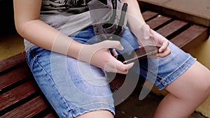 Child Playing Video Games on a Smartphone in Park Outdoors, Sitting on a Bench