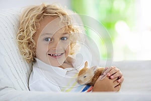 Child playing with white rabbit. Little boy feeding and petting white bunny. Easter celebration. Egg hunt with kid and pet animal