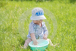 Child plays with a basin of water on the grass. Funny Baby Boy Playing Outside with Water and Bubbles. A cute baby boy is making a