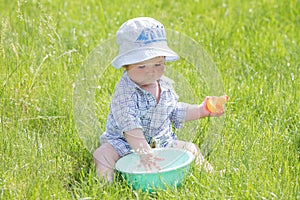 Child plays with a basin of water on the grass. Funny Baby Boy Playing Outside with Water and Bubbles. A cute baby boy is making a