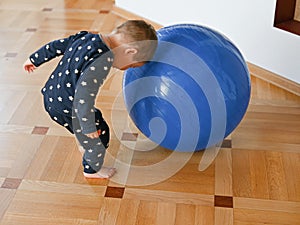 Child plays with a big blue ball. Developing motor skills. Baby plays