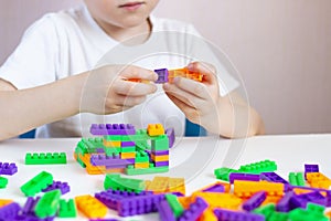 A child plays with a bright constructor on a white table. Children`s creativity quarantined. Hands large board