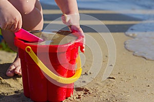 The child plays with a bucket and sand on the seashore in summer day