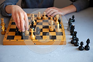 A child plays chess alone. Old wooden chessboard. Children`s hands. Chess pieces on a chessboard