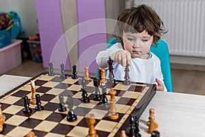 The child plays with the figures on a wooden chessboard