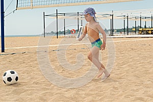 The child plays football on the beach.