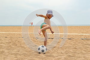 The child plays football on the beach.