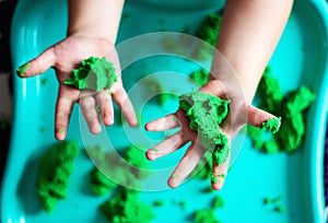 A child plays with kinetic sand. Hands of a child playing with green magic sand. Children`s creativity. Kinetic sand in a green