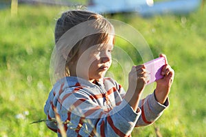 Child plays photographer outdoors. Girl imagines taking pictures on pink plastic toy phone