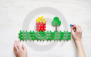 Child plays with the plastic designer. Hands of the child and image of the house and trees.