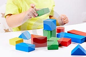 A child plays with playful colored geometric shapes on a light table. The child builds towers from toy building bricks