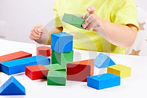 A child plays with playful colored geometric shapes on a light table. The child builds towers from toy building bricks
