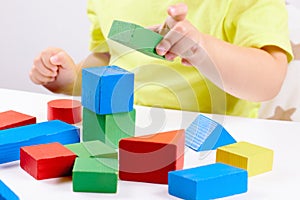 A child plays with playful colored geometric shapes on a light table. The child builds towers from toy building bricks