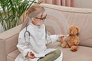 Child plays profession of doctor and feeds the toy teddy bear toy from a spoon.