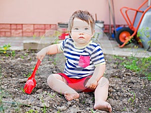Child plays with a red children`s spatula. Little boy delves into the ground