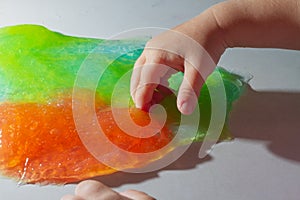 The child plays with a red and green slime, the baby crushes the slime with his hand