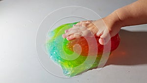 The child plays with a red and green slime, the baby crushes the slime with his hand