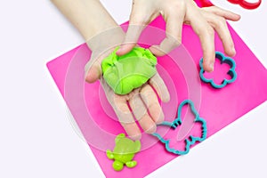 The child plays and sculpts figures from soft green plasticine on a pink board
