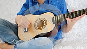 A child plays a small guitar close up. Playing the guitar, singing, music, education, rhythm.