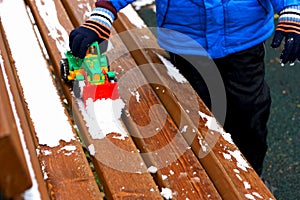 The child plays with the snow on the bench.