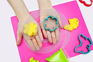 The child plays with soft plasticine and sculpts different figures on a pink board