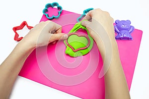 The child plays with soft plasticine and sculpts a green heart using the shape