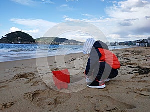 a child plays with a paddle and a bucket on the beach in cold weather photo