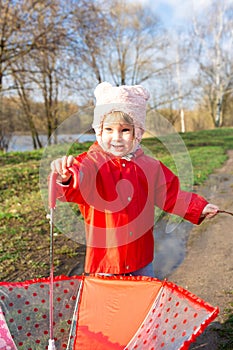 Child plays with umbrella after the rain in red rubber boots and a raincoat.