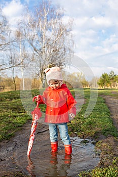 Child plays with umbrella after the rain in red rubber boots and a raincoat.