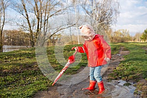 Child plays with umbrella after the rain in red rubber boots and a raincoat.