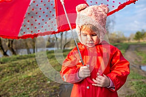 Child plays with umbrella after the rain in red rubber boots and a raincoat.
