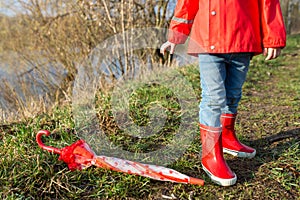 Child plays with umbrella after the rain in red rubber boots and a raincoat.