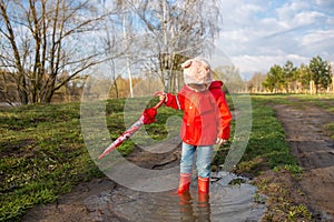 Child plays with umbrella after the rain in red rubber boots and a raincoat.