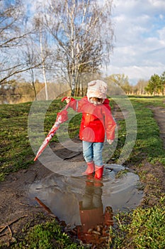 Child plays with umbrella after the rain in red rubber boots and a raincoat.