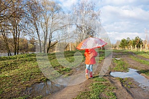 Child plays with umbrella after the rain in red rubber boots and a raincoat.