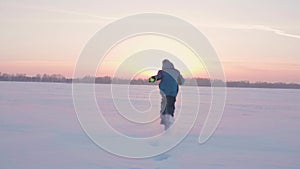 A child plays in the winter outdoors, runs, throws snow to the top. Beautiful sunset. Active outdoor sports