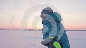 A child plays in the winter outdoors, runs, throws snow to the top. Beautiful sunset. Active outdoor sports