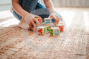 child plays with wooden blocks with letters on the floor in the room a little girl is building a tower at home or in the